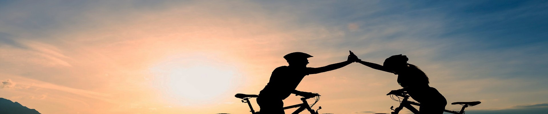 Two cyclists with raised arms with light shining towards the viewer