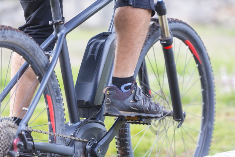 E bisiklet Siyah bir e-bisikletin pedallarında görünen bacaklar ve spor ayakkabı