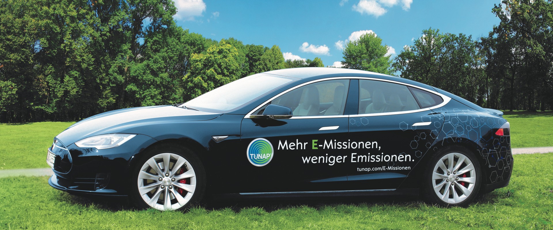 Side view of a dark blue sports car with white lettering and a TUNAP logo on a green meadow