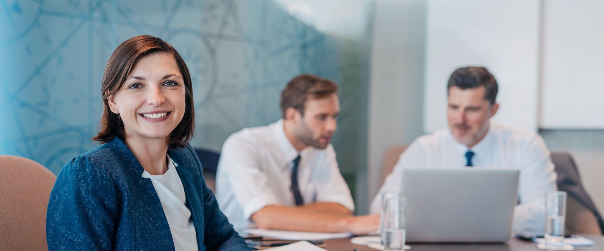 Portrait of a smiling young businesswoman sitting at a table with colleagues working in the background